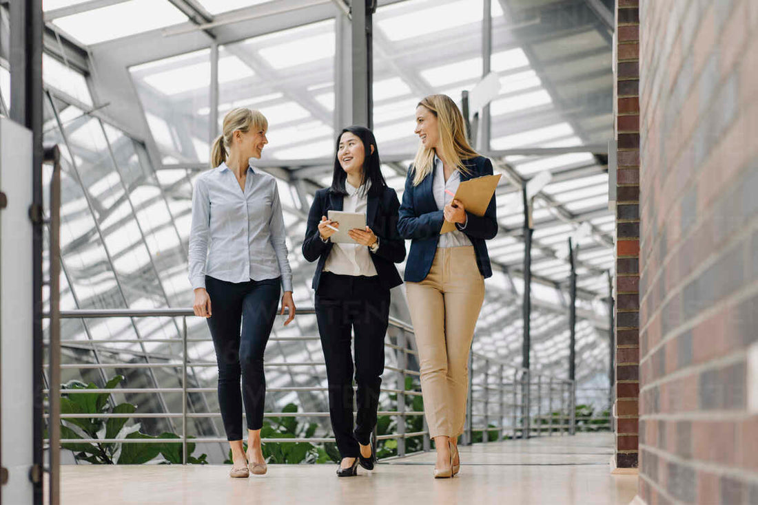 three women walking through office building looking at each other and talking